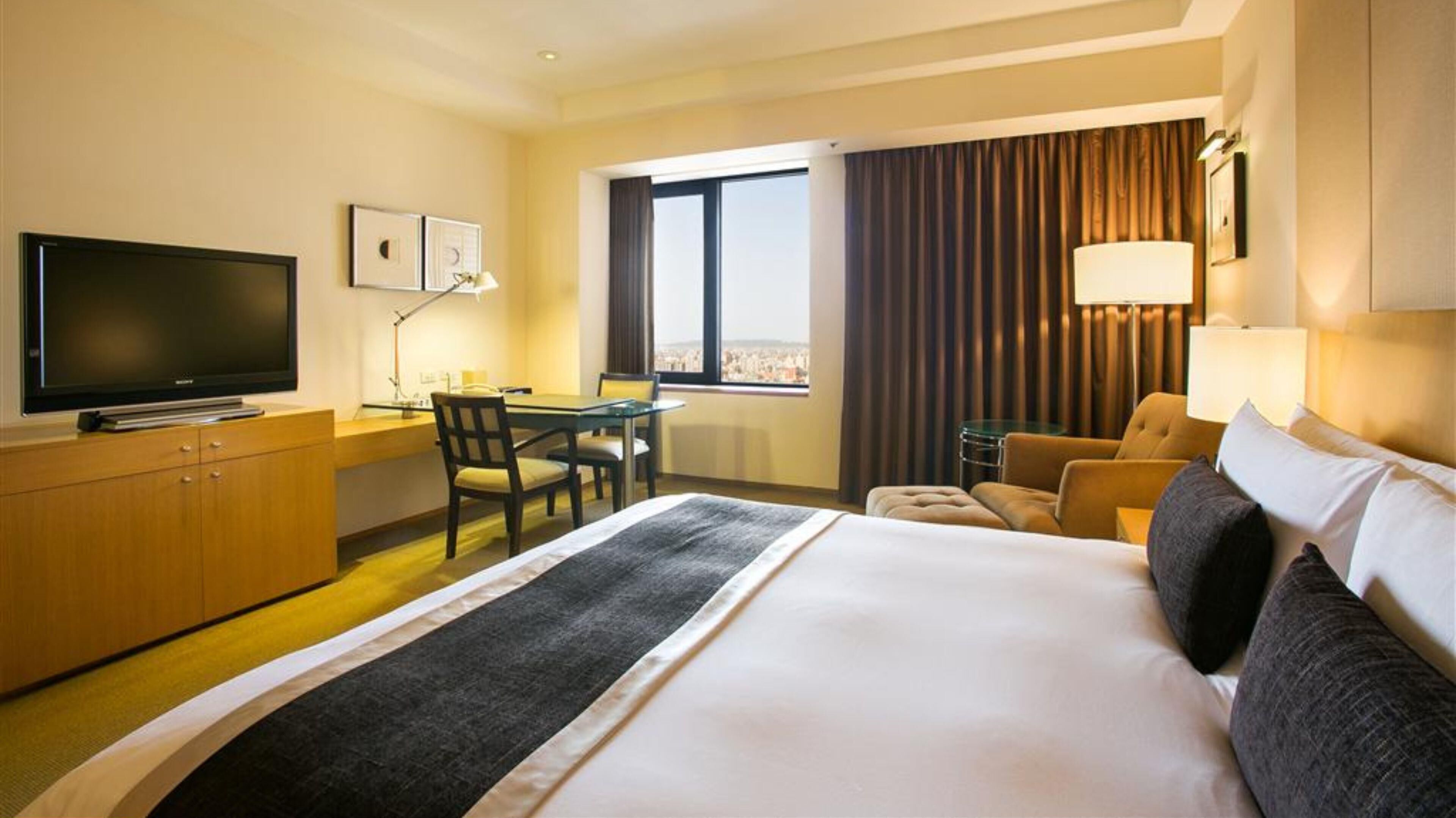 Una habitación de hotel con una cama grande, un escritorio con silla, un televisor y una ventana con cortinas.