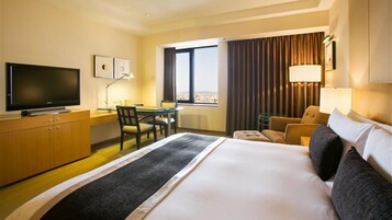 Una habitación de hotel con una cama grande, un escritorio con silla, un televisor y una ventana con cortinas.