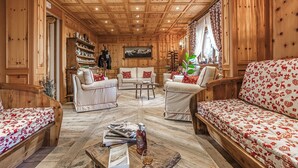 A wooden-paneled room with a sofa, chairs, a coffee table, and a bookshelf.