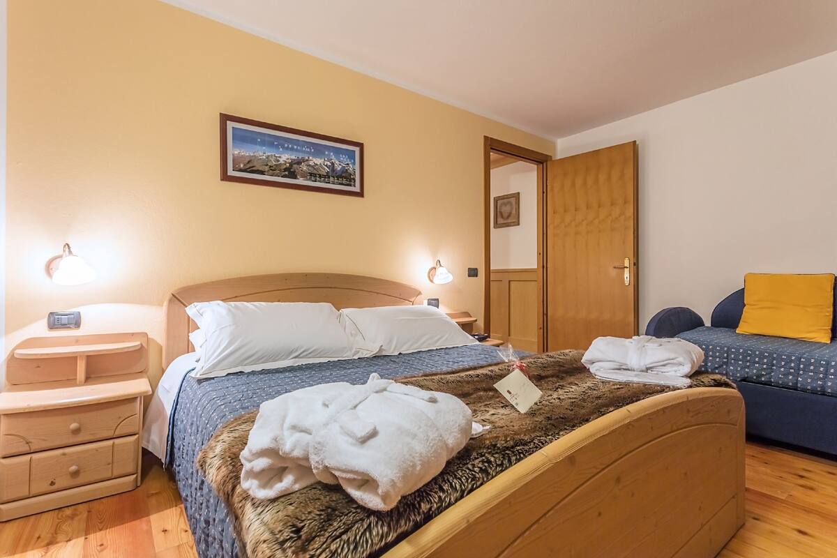 Ein Schlafzimmer mit einem hölzernen Bett, einem Nachttisch, einer Lampe, einem gerahmten Bild an der Wand und einer Tür zu einem anderen Raum.