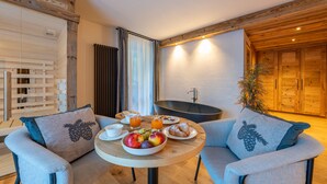 A cozy room with a round wooden table set with breakfast, two armchairs, a bathtub, and wooden walls.