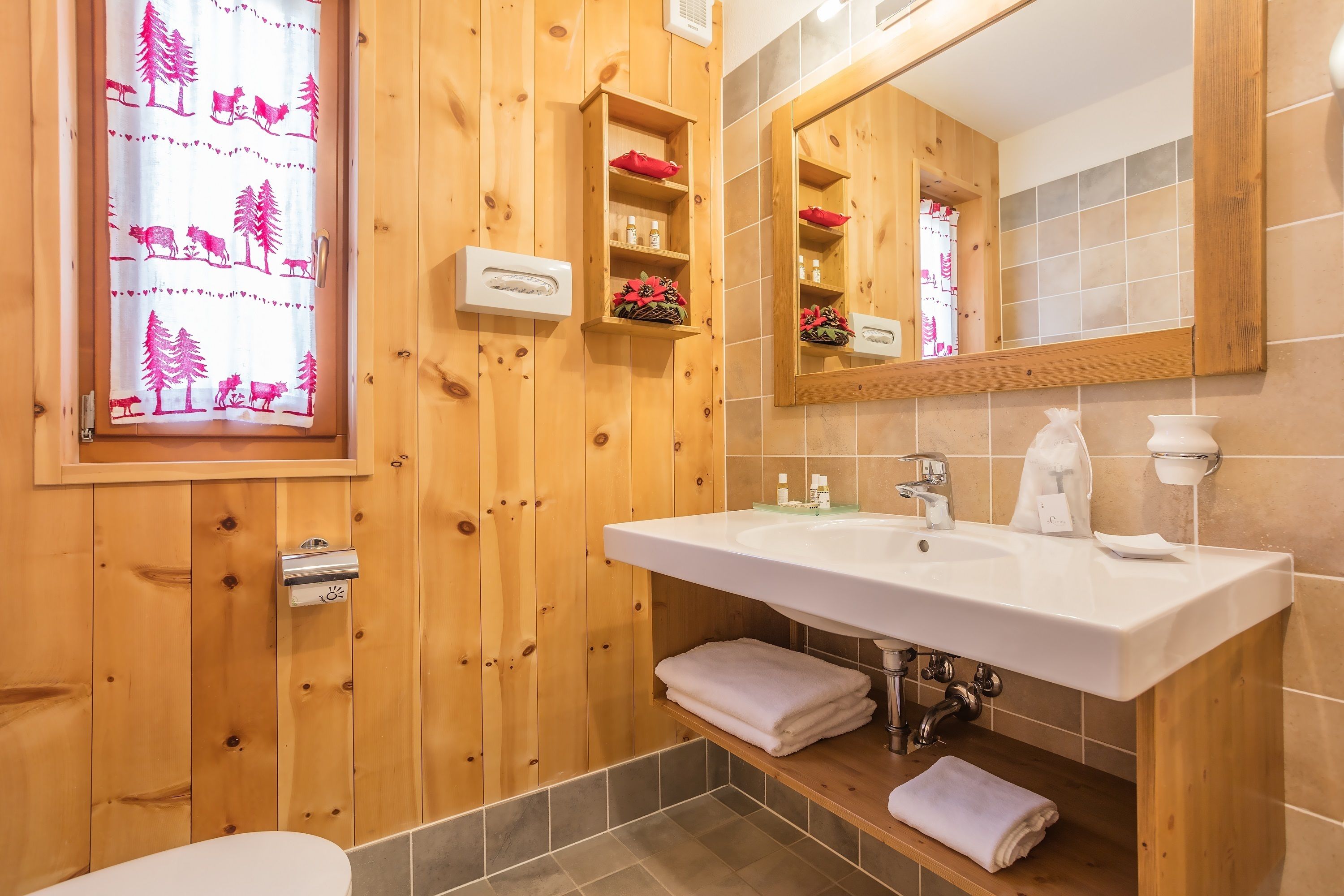 A wooden-paneled bathroom with a large mirror, a sink, and a window with a curtain featuring animal prints.