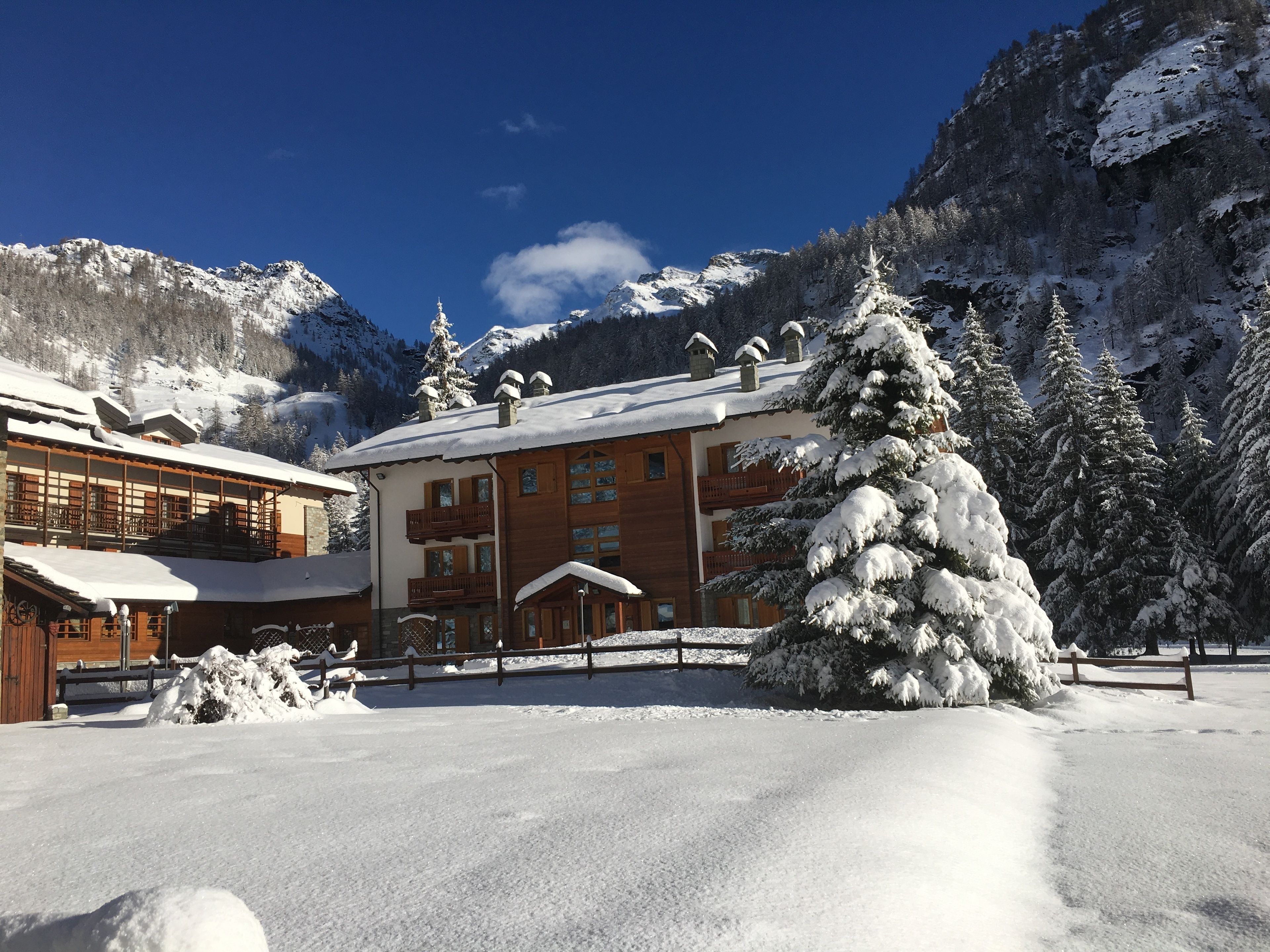 Un lodge imbiancato dalla neve, con facciata in legno, ampie finestre e un balcone affacciato su un paesaggio innevato.