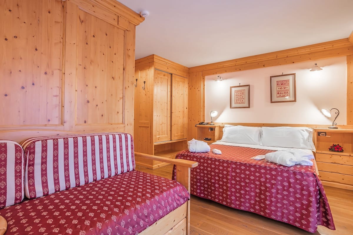 Ein schlicht eingerichtetes Schlafzimmer im Blockhausstil mit zwei Betten, einem Holzschrank und einer Bank.
