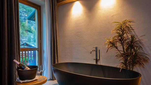 A modern bathroom with a large black bathtub, a potted plant, and a window with curtains.