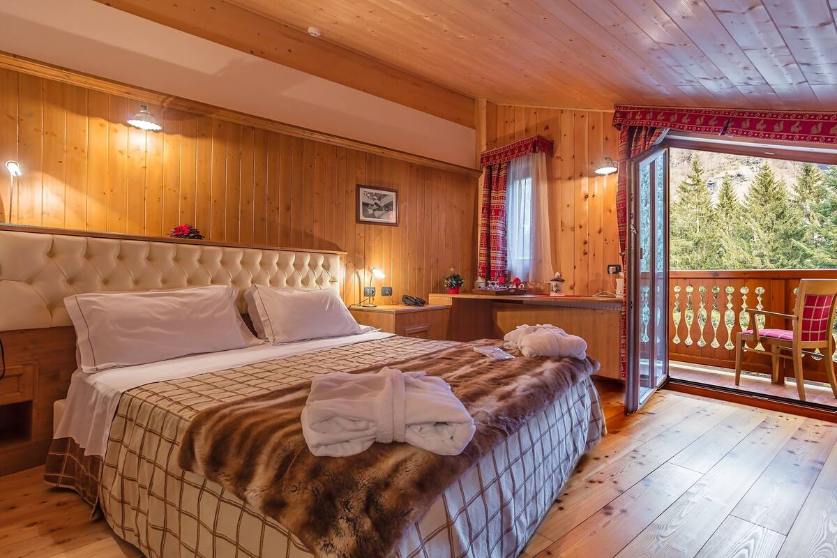 Ein Schlafzimmer mit Holzwänden, einem Bett, einem Nachttisch und Blick ins Freie.