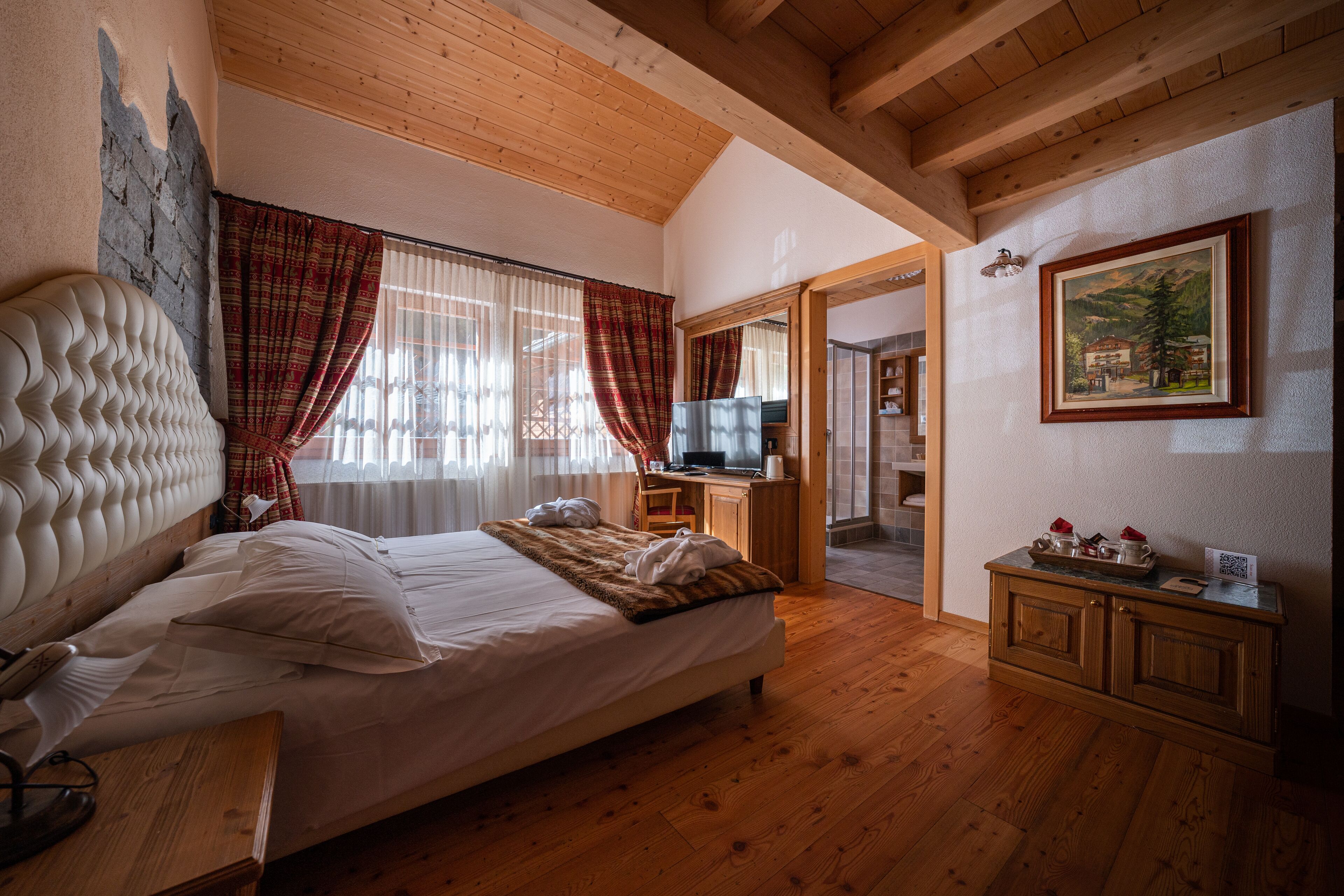 Ein Schlafzimmer mit einem großen Bett, Holzbalkendecke, einem Schreibtisch und einem Spiegel.