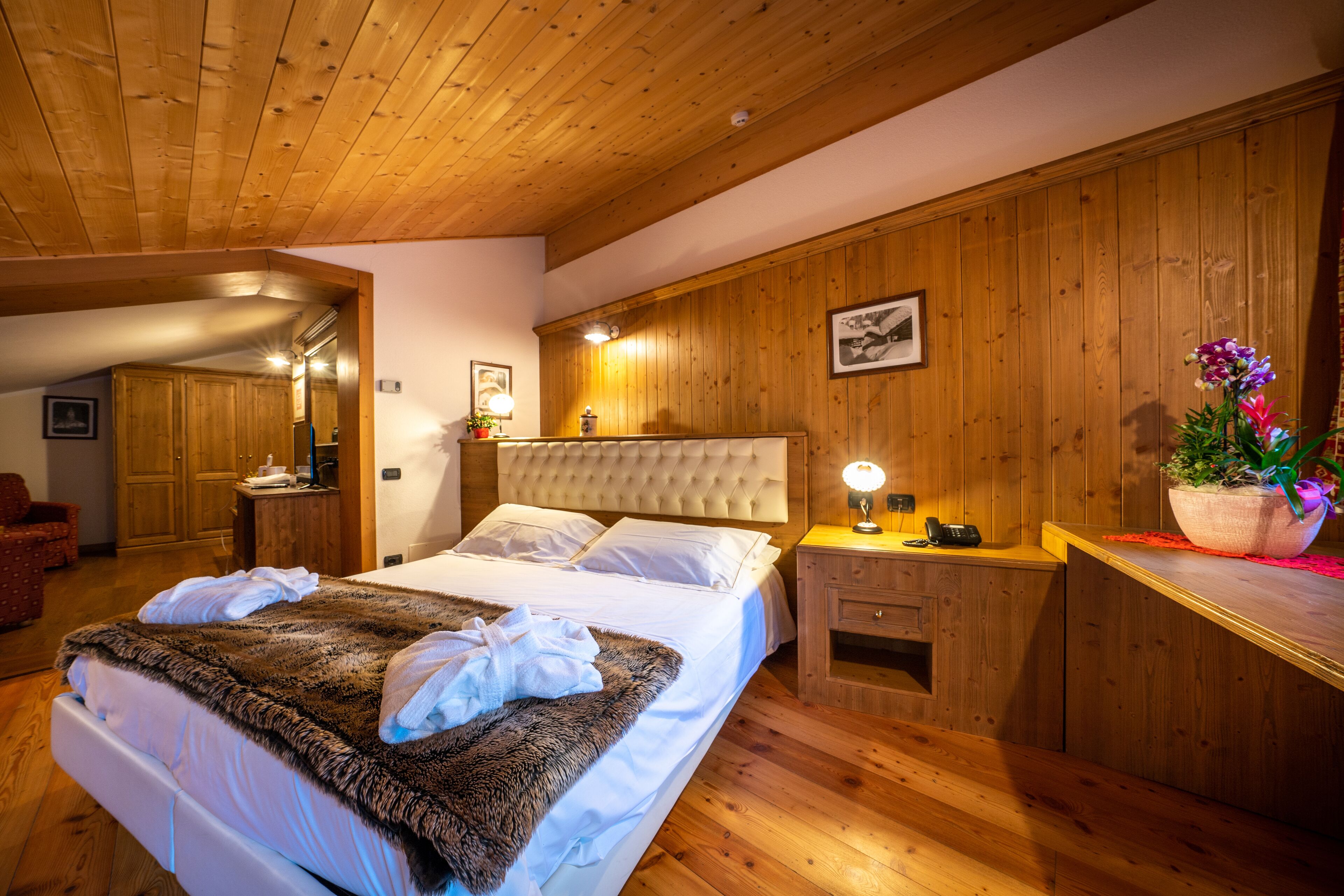 Una camera da letto con un letto grande, pareti in legno, una testiera, comodini e una pianta in vaso.