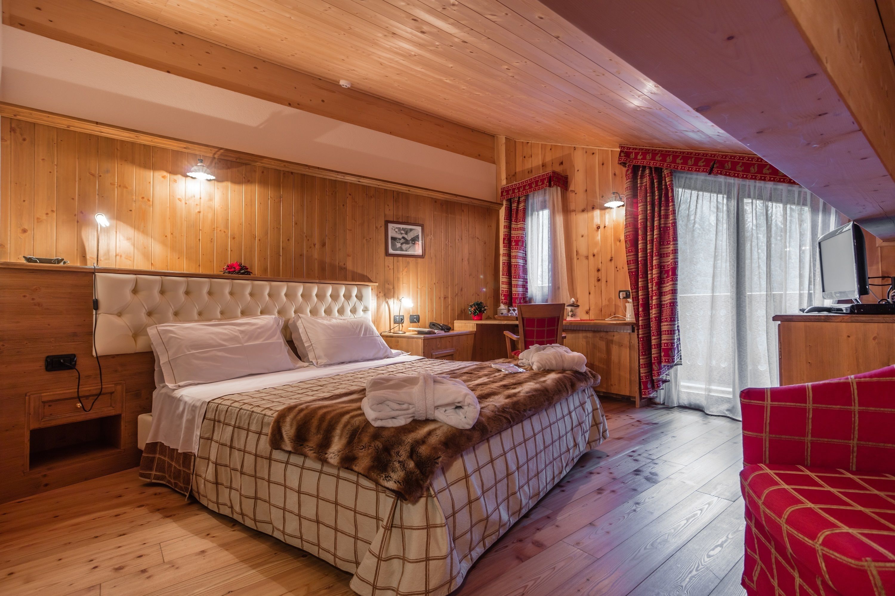 Une chambre aux murs lambrissés, avec un grand lit, un bureau et un téléviseur.