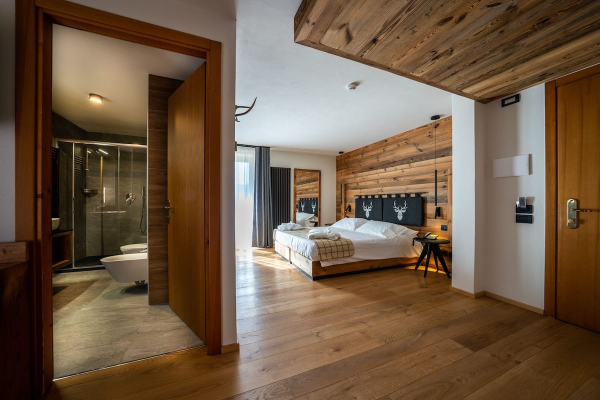 Ein modernes Schlafzimmer mit Holzboden, einem großen Bett, einem Nachttisch und Blick ins Badezimmer.