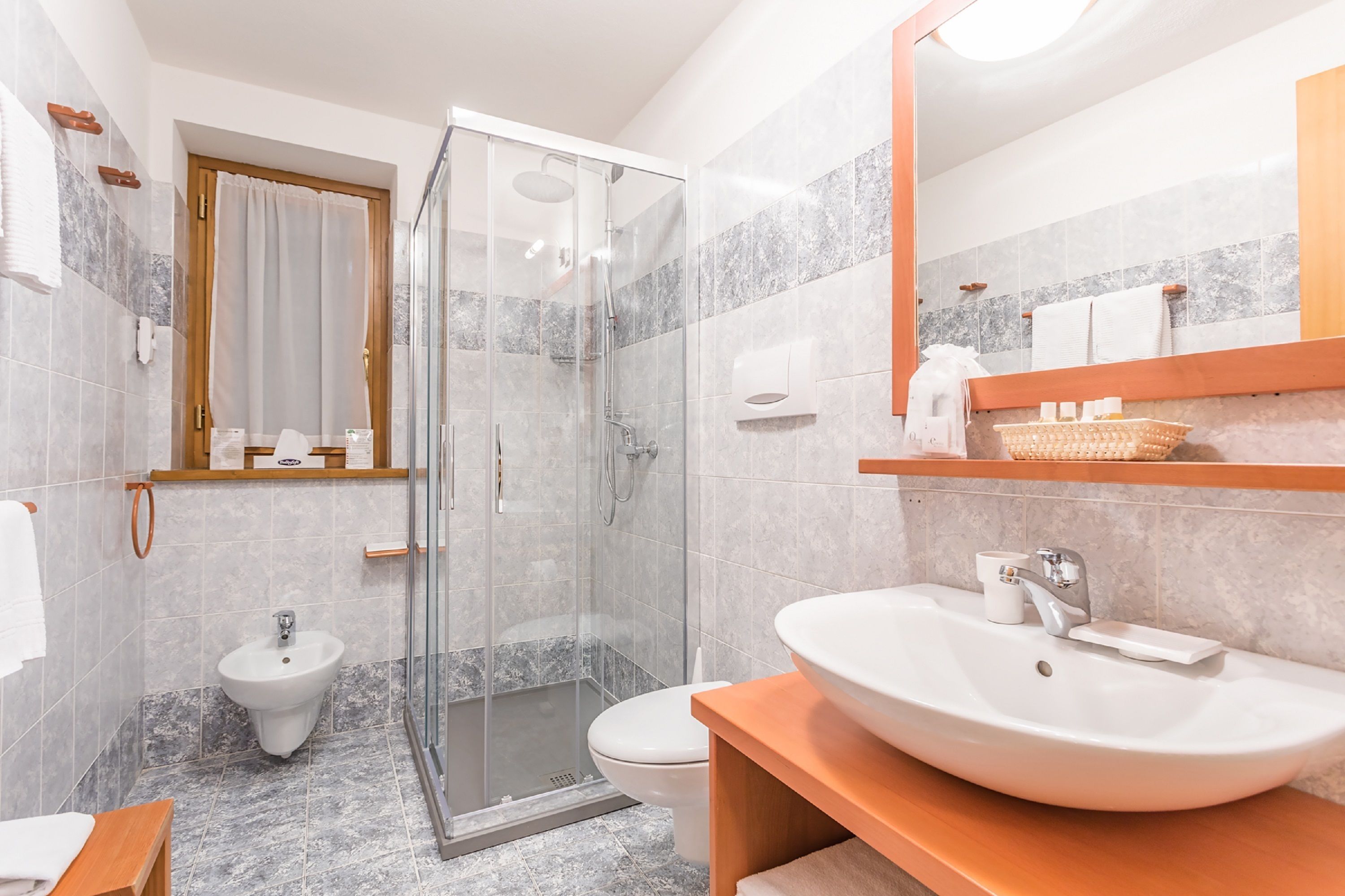 A modern bathroom with a glass-enclosed shower, a pedestal sink, and a large mirror.