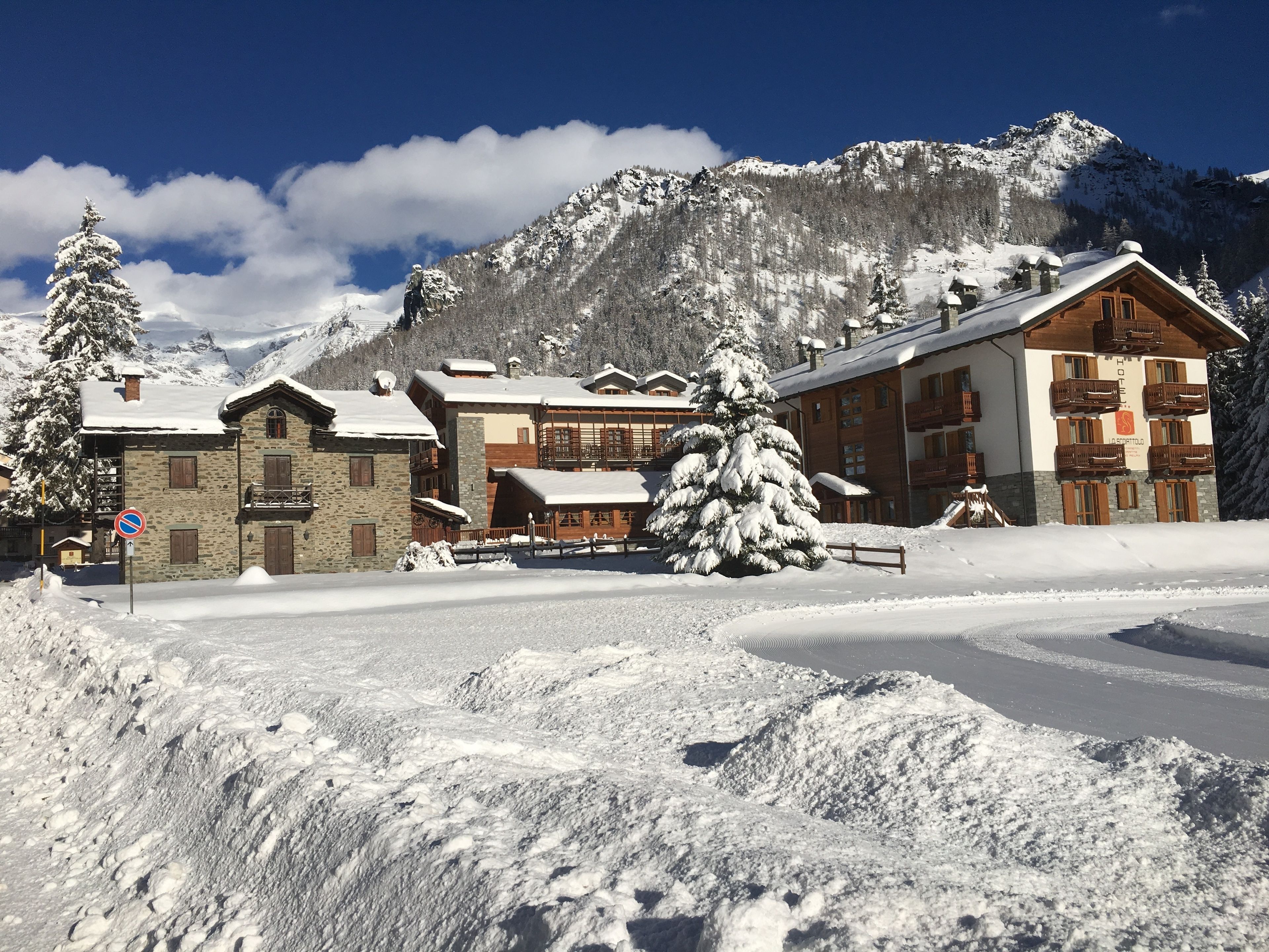 Ein mit Schnee bedecktes Berghotel mit Stein- und Holzarchitektur, eine Seilbahn und ein freier Blick auf die umliegenden Berge.