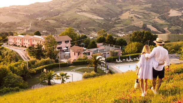 A couple overlooking a pool with a view of a residential area and hills in the background. - I Calanchi Country Hotel & Resort (Ripatransone)