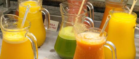 A variety of colorful beverages in glass pitchers with straws, placed on a marble surface.