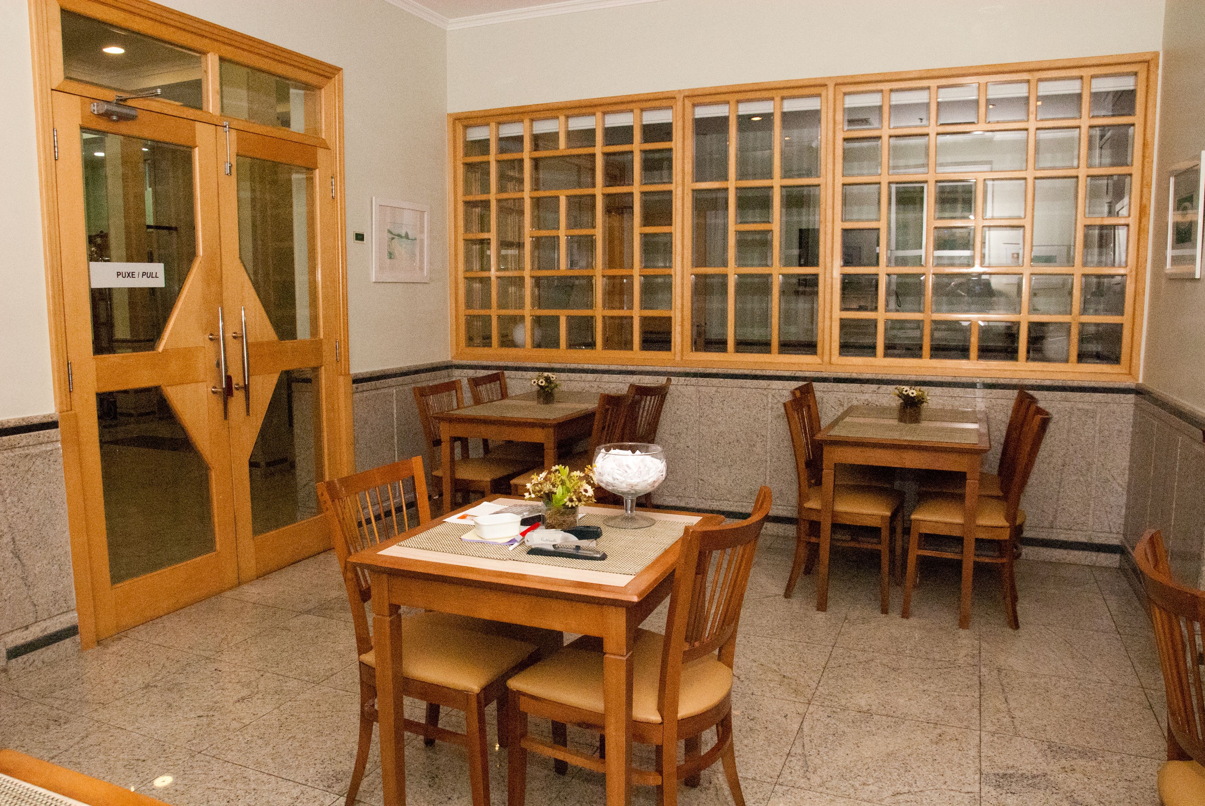 A dining area with wooden tables and chairs, a large window with multiple panes, and a door with a sign indicating 'PUKE / PULL'.