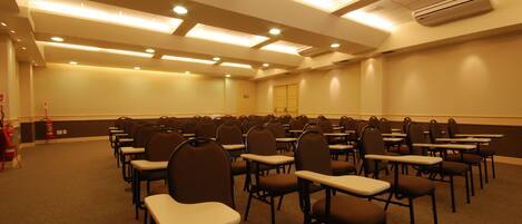 A conference room with rows of chairs and tables, ceiling lights, and an air conditioning unit.