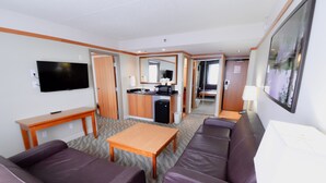 Habitación de hotel con sofá, una mesita, televisor, kitchenette y espejo.