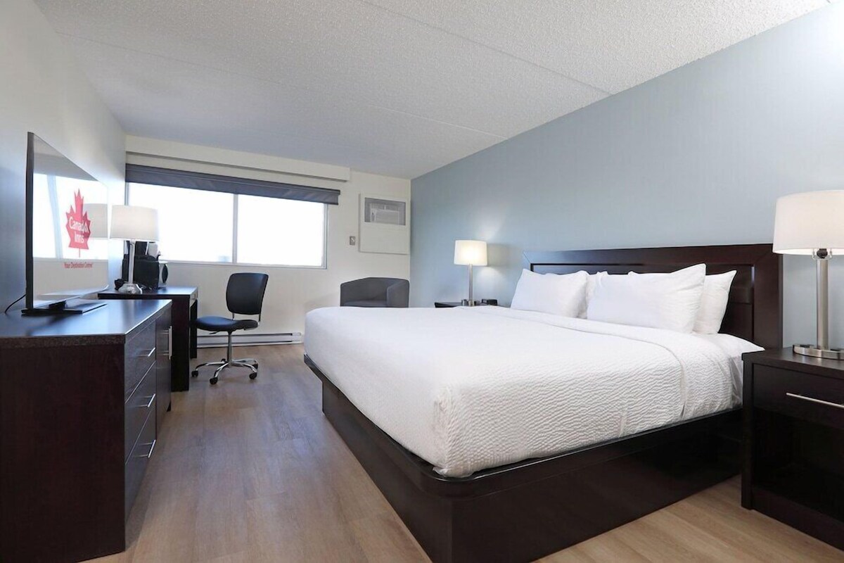 A hotel room with a bed, desk, chair, and lamps.