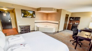 Habitación de hotel con una cama grande, baño independiente con bañera, escritorio con silla y una kitchenette pequeña.