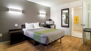 Une chambre d’hôtel moderne, équipée d’un lit, de tables de chevet, d’un miroir et d’une porte donnant accès à une salle de bain.