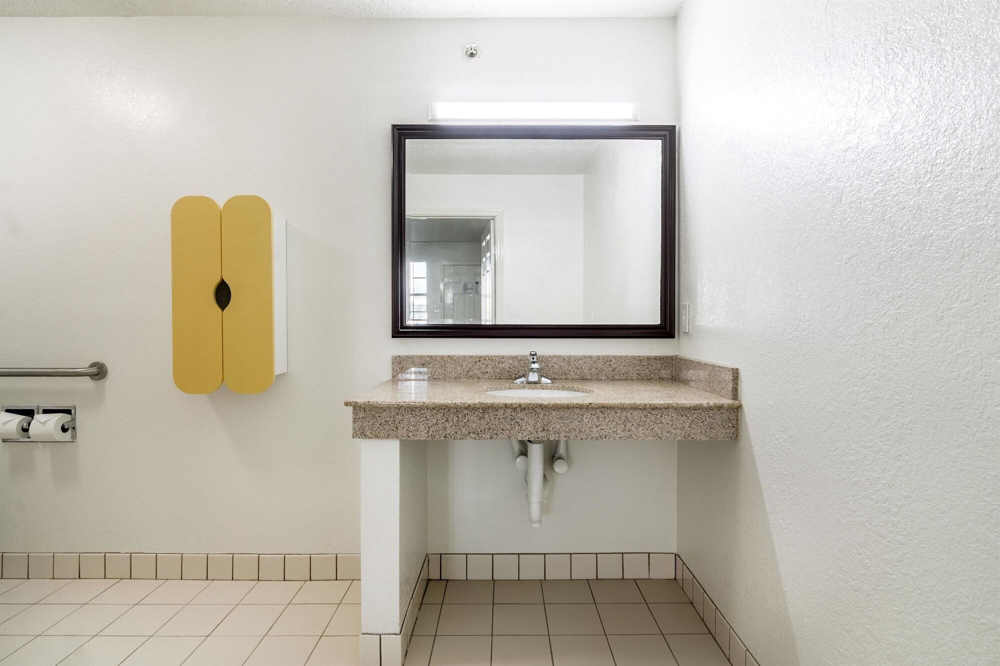 A bathroom with a white tiled floor, a granite countertop sink, a mirror, and a toilet paper holder.
