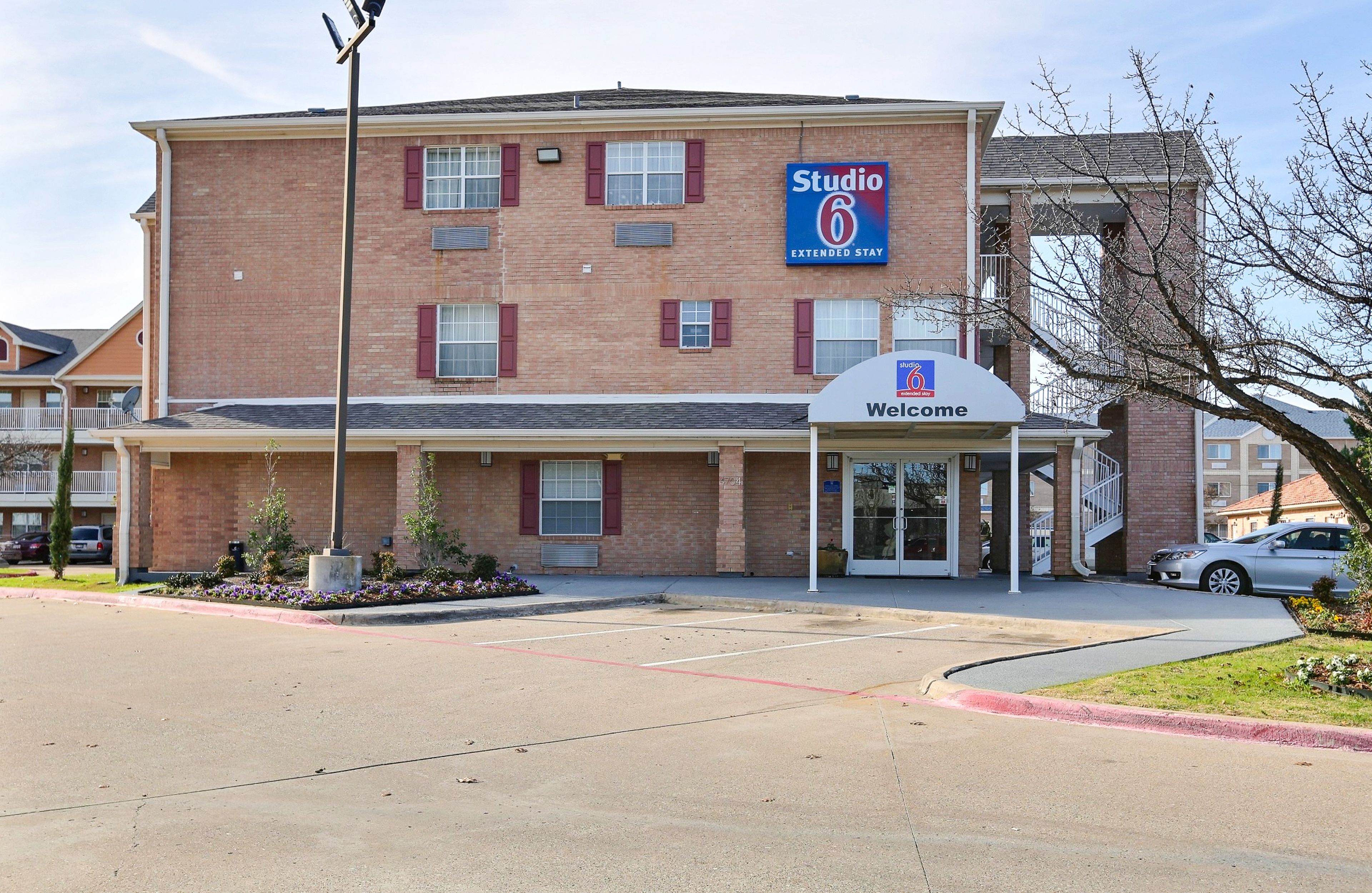 A Studio 6 Extended Stay hotel with a brick facade, a 'Welcome' entrance, and a parking lot.