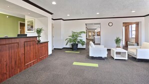 Un espace d’accueil avec un bureau en bois, deux plantes en pot, des canapés blancs et une horloge au mur.