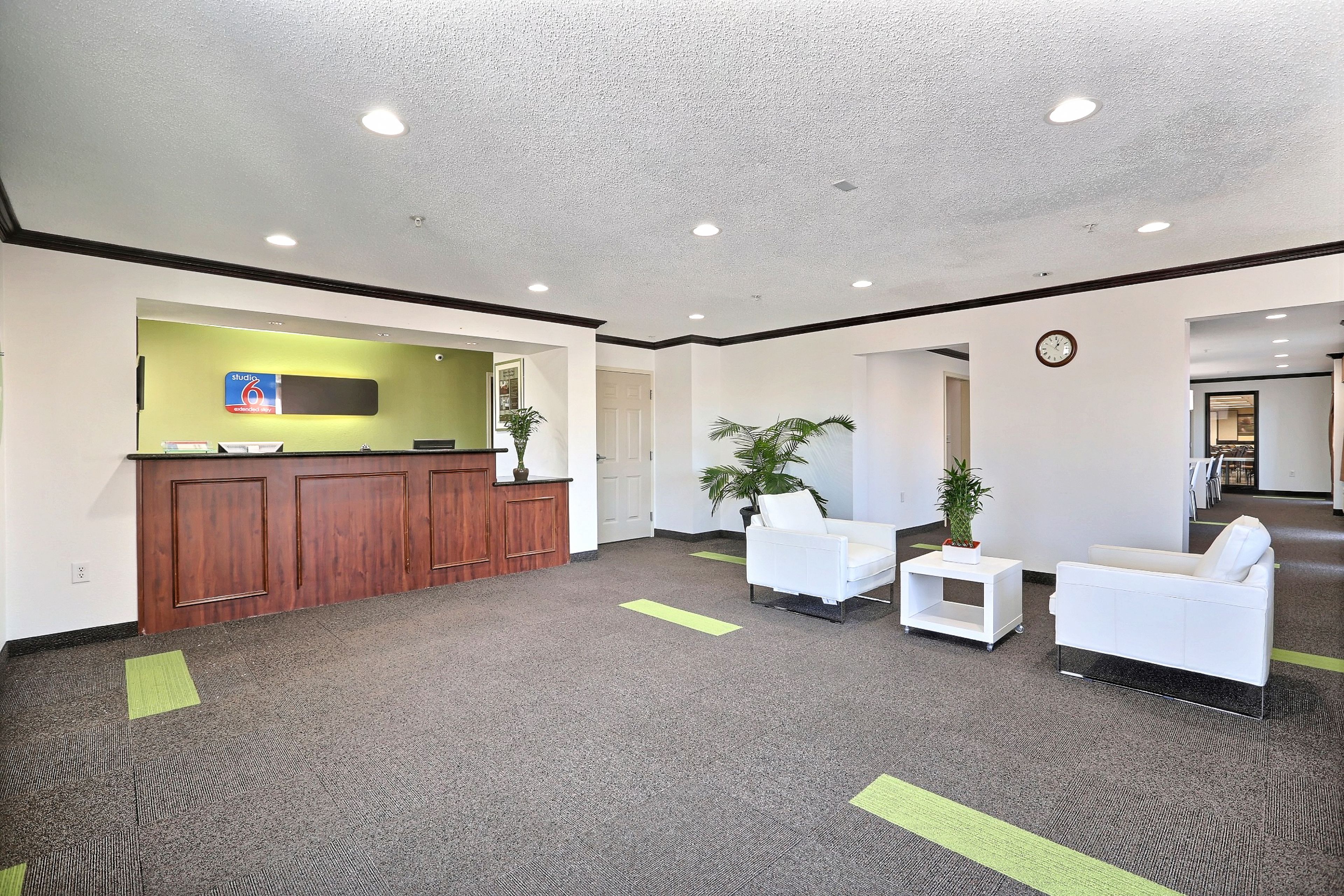 A reception area with a wooden desk, white chairs, and a potted plant.