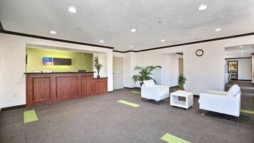 A reception area with a wooden desk, white chairs, and a potted plant.
