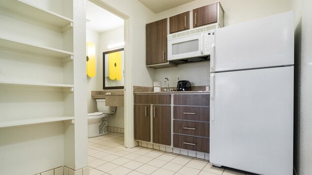 A compact kitchen with a white refrigerator, a microwave, and a sink. There are wooden cabinets and a toilet visible in the background.