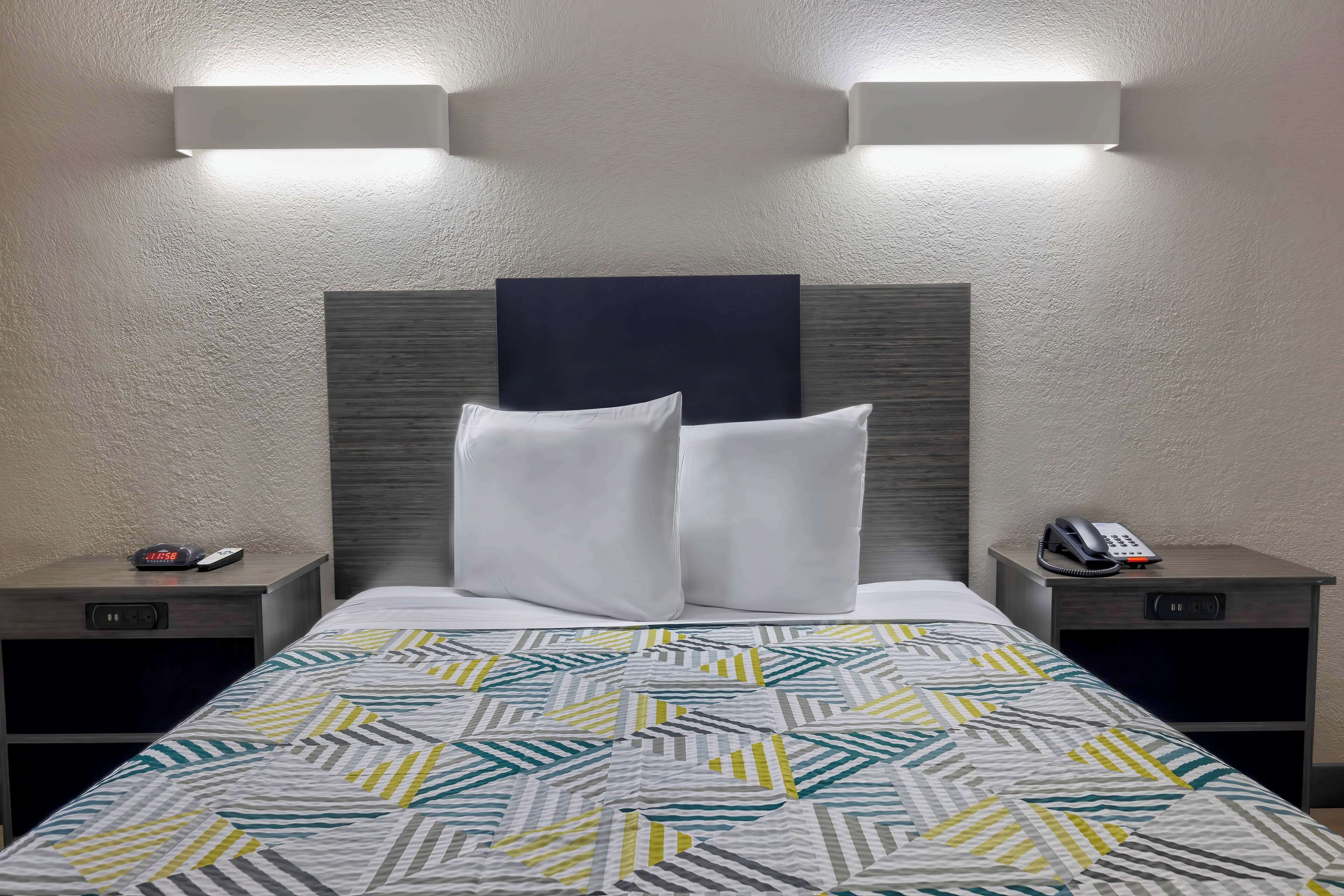 Una camera d'albergo con un letto, due comodini, un telefono a parete e un punto luce a parete.