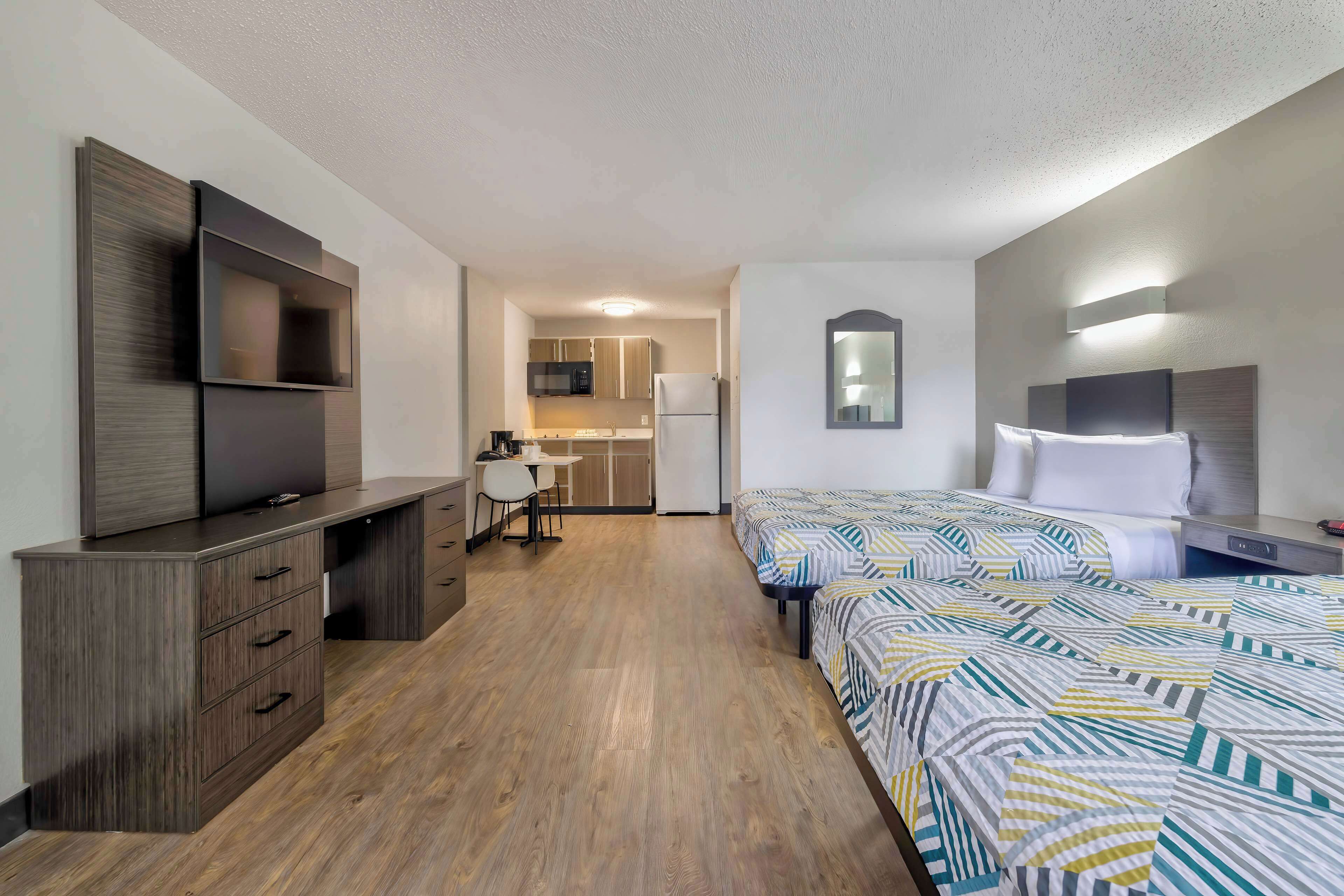 Une chambre d’hôtel équipée d’un bureau, de deux lits, d’une télévision et d’une kitchenette.