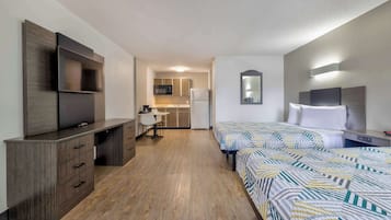 Une chambre d’hôtel équipée d’un bureau, de deux lits, d’une télévision et d’une kitchenette.