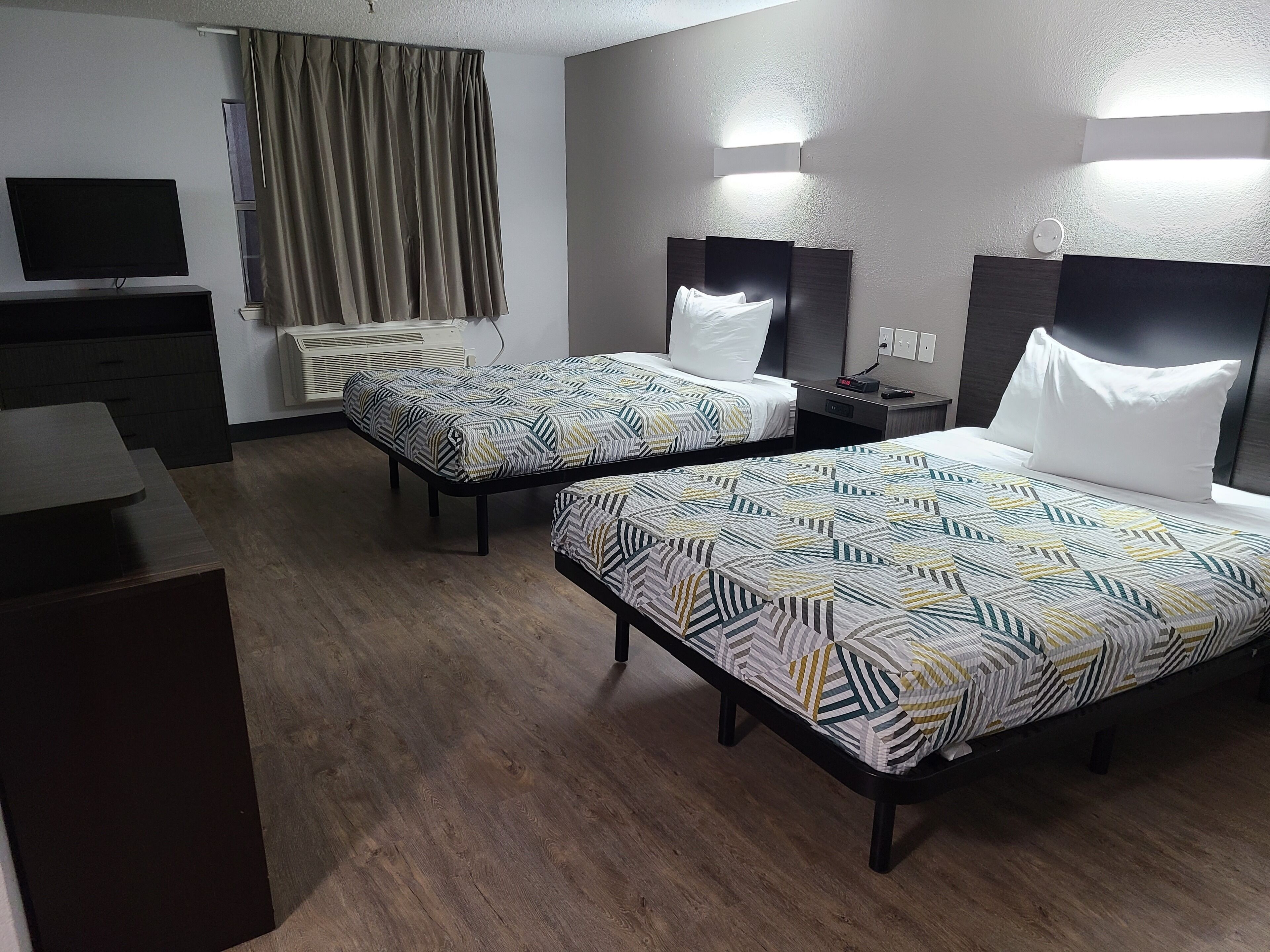 A hotel room with two beds, a TV, a desk, and a window with curtains.