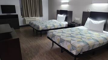 A hotel room with two beds, a TV, a desk, and a window with curtains.