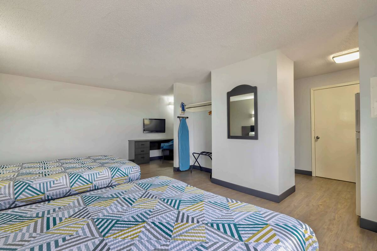 A hotel room with two beds, a desk, a TV, and a mirror.