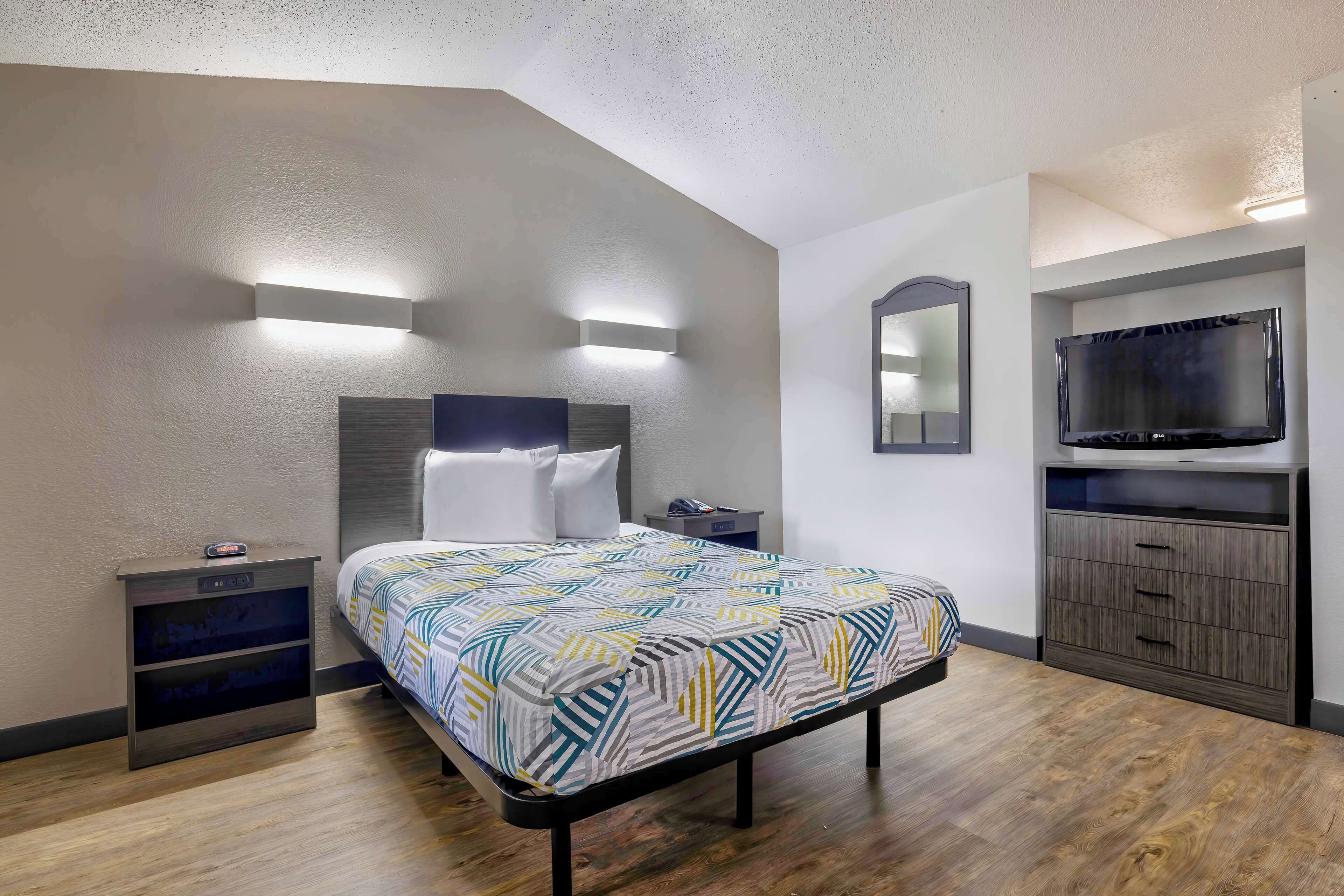 A modern hotel room with a bed, bedside tables, a TV, and built-in storage.