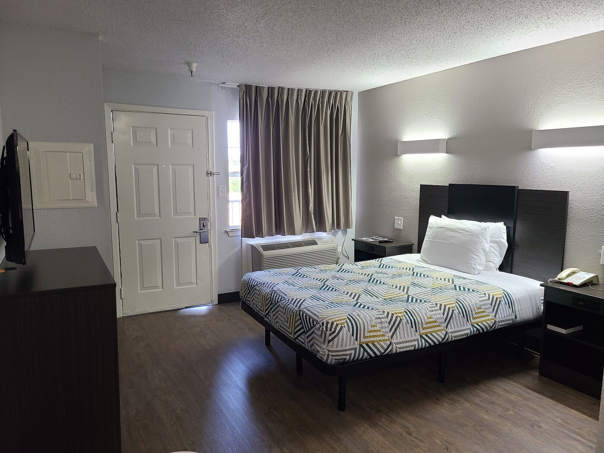 A hotel room with a bed, bedside table, lamp, and a door.