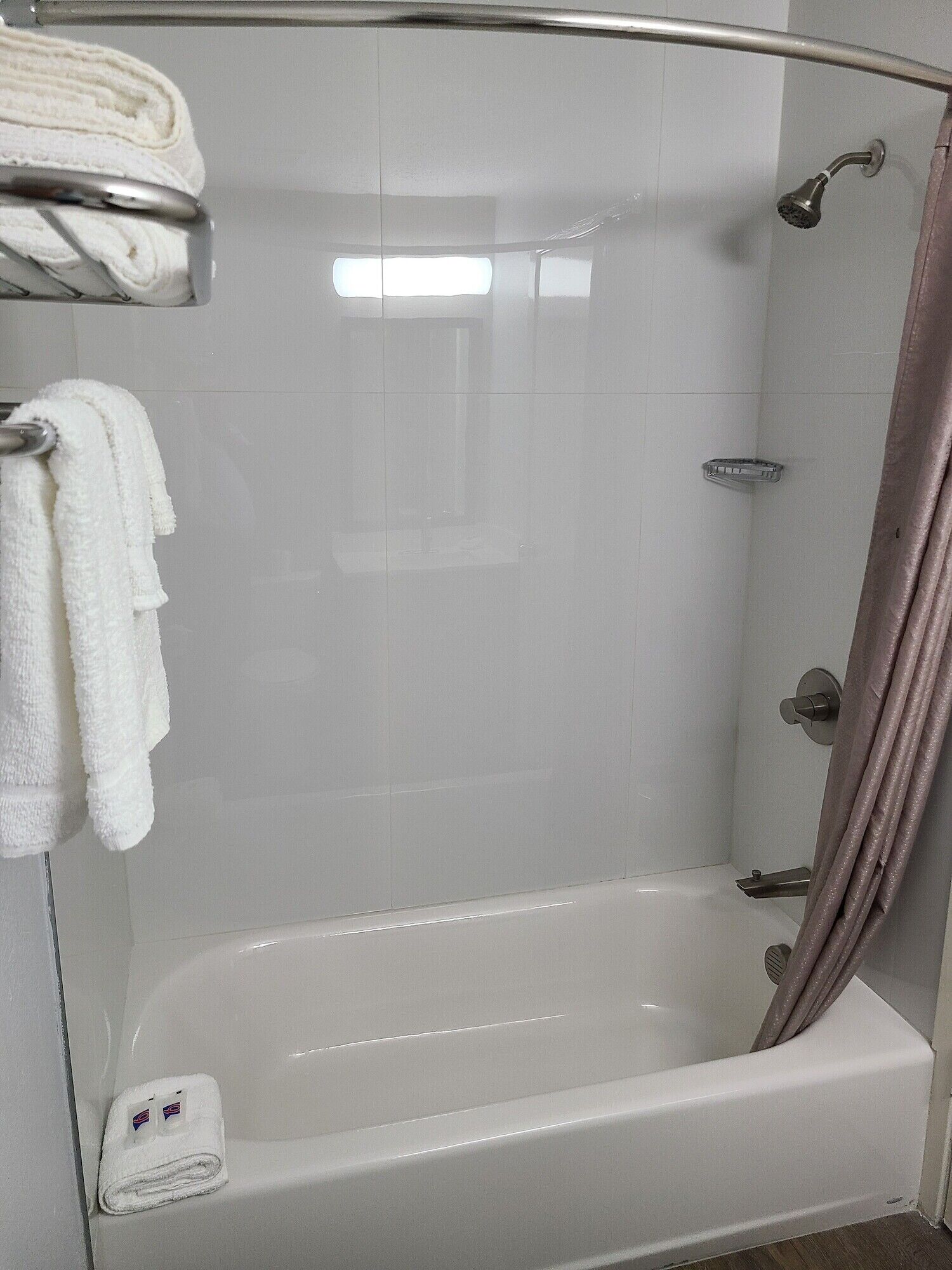 Una doccia con porta in vetro, una vasca da bagno bianca e un portasciugamani con asciugni piegati.