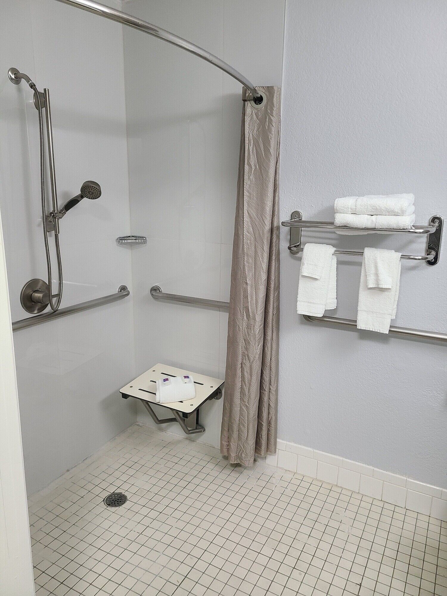 A walk-in shower with a showerhead, handheld shower, and a small bench.