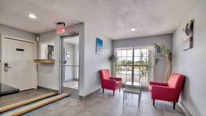 A reception area with a glass door, red chairs, a small table, and a striped rug. - Studio 6 Dallas, TX - North - Richardson (Dallas)