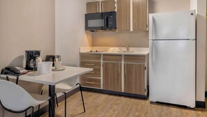 A compact kitchenette with a microwave, refrigerator, and a small dining area with a table and chairs. - Studio 6 Dallas, TX - North - Richardson (Dallas)