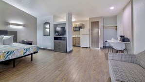 A modern hotel room with a bed, a sofa, a kitchenette, and a dining area. - Studio 6 Dallas, TX - North - Richardson (Dallas)