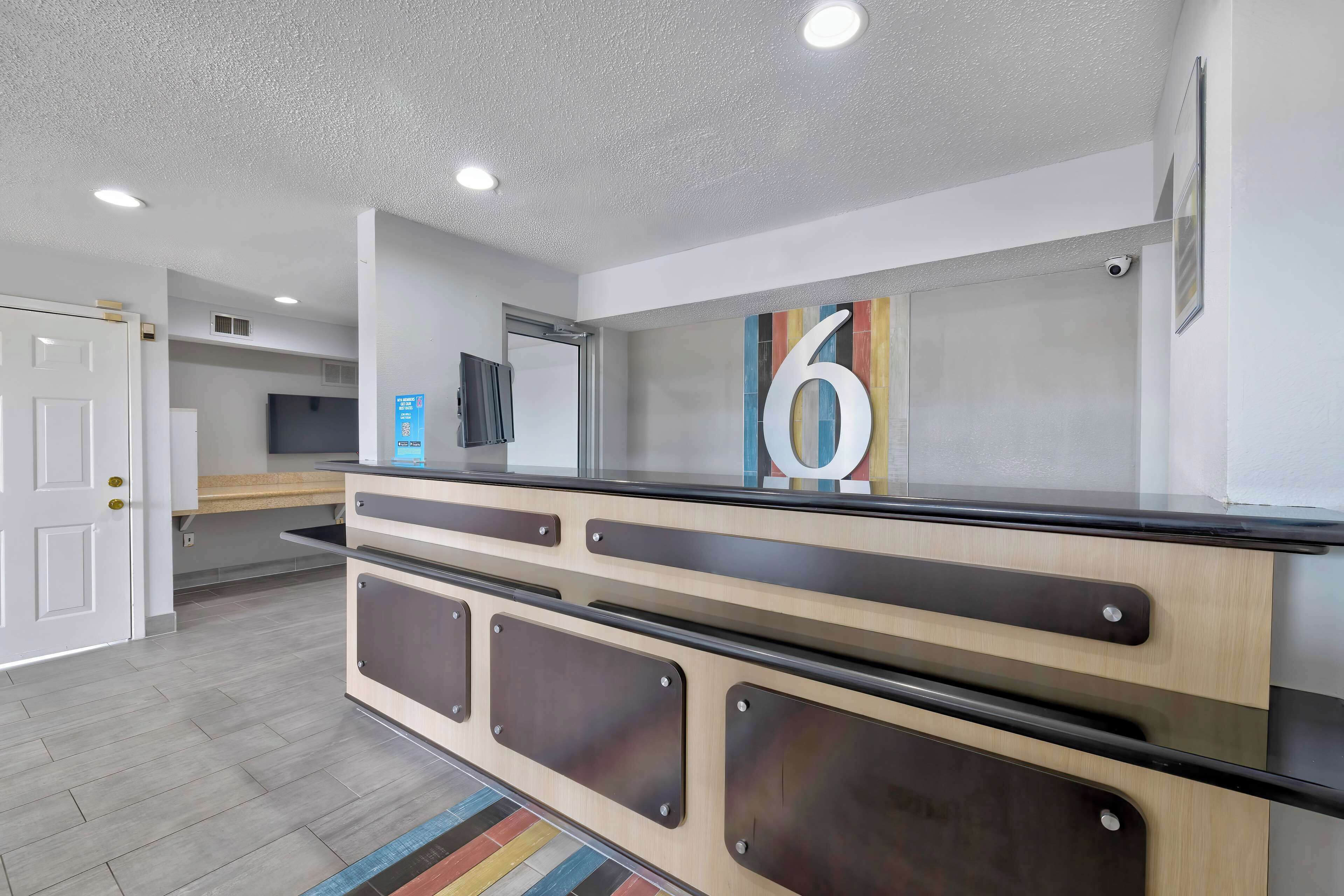 A modern reception desk with a large number '6' sign, a flat-screen TV, and a security camera.