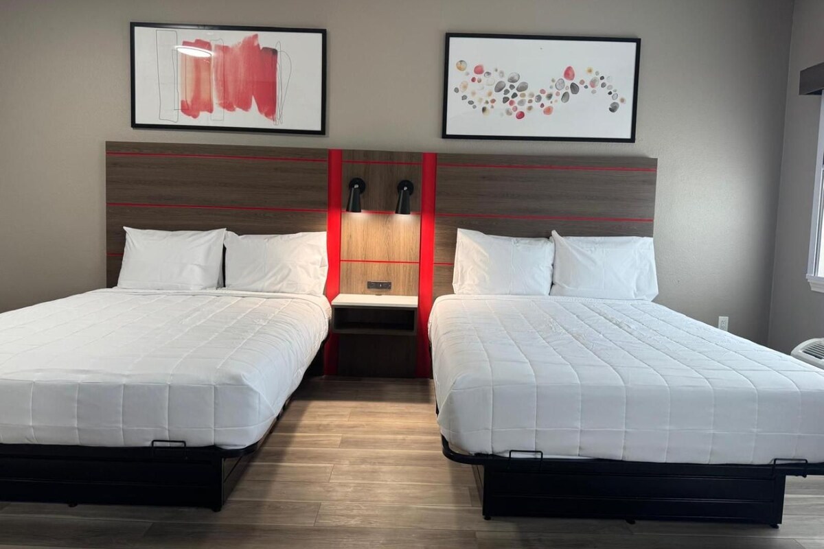 Una habitación de hotel con dos camas, un cabecero de madera y dos cuadros enmarcados en la pared.