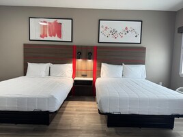 A hotel room with two beds, a wooden headboard, and two framed artworks on the wall.