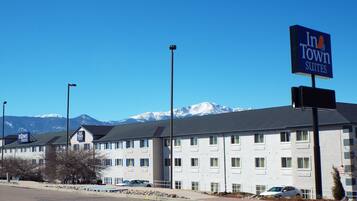 A hotel with multiple floors, a prominent InTown Suites sign, and a view of snow-capped mountains in the background.