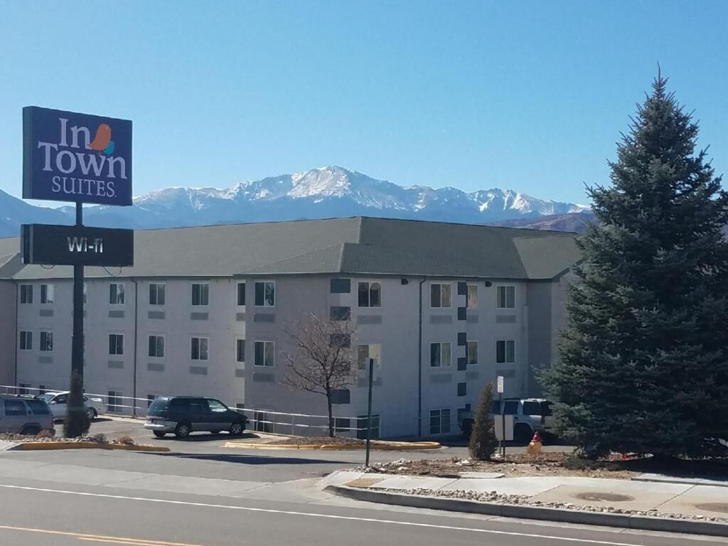 A hotel with a sign for In Town Suites, Wi-Fi availability, and a view of snow-capped mountains in the background.