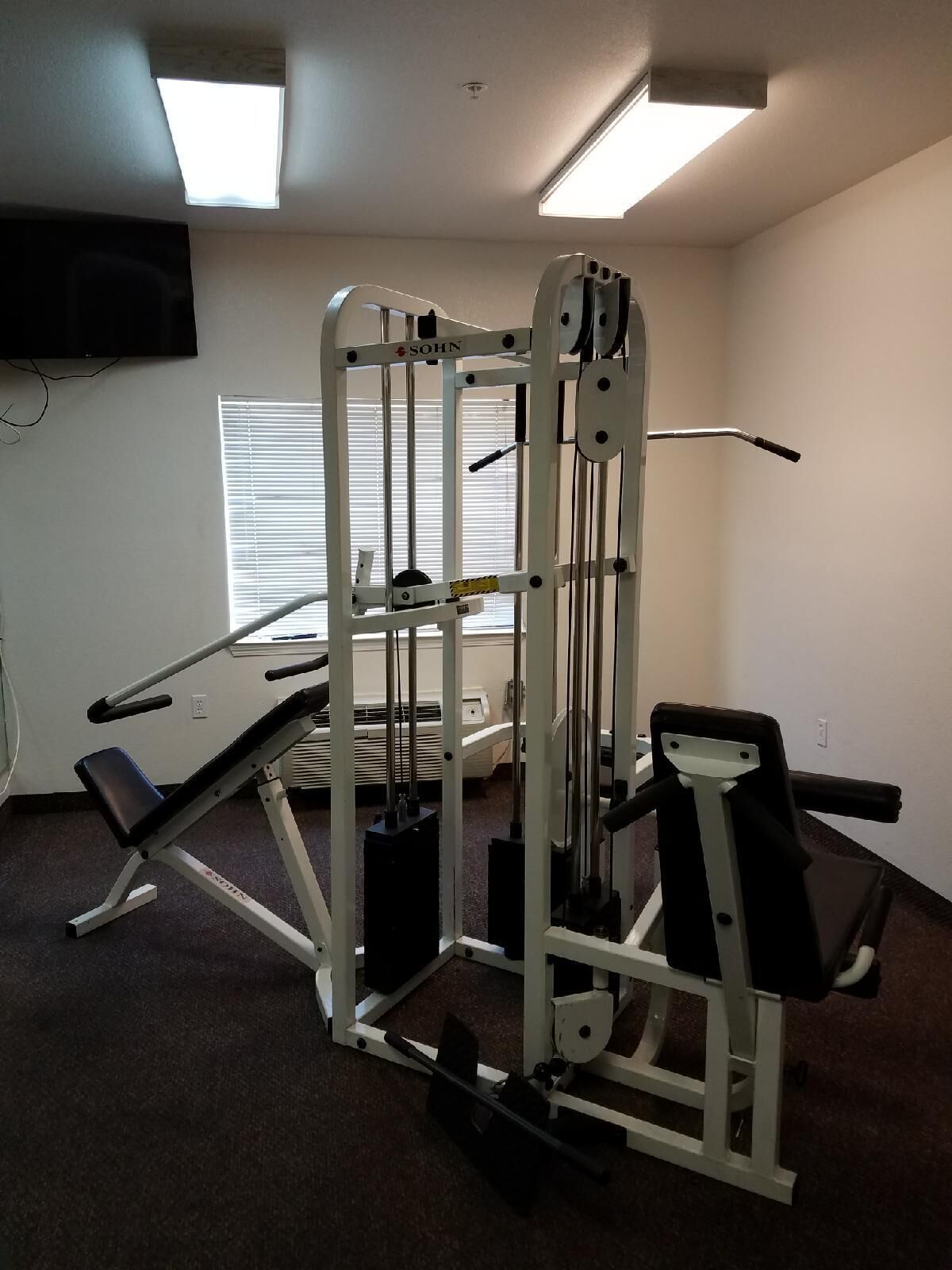 Ein Fitnessraum mit einer Smith-Maschine, Bänken und einem Spiegel.