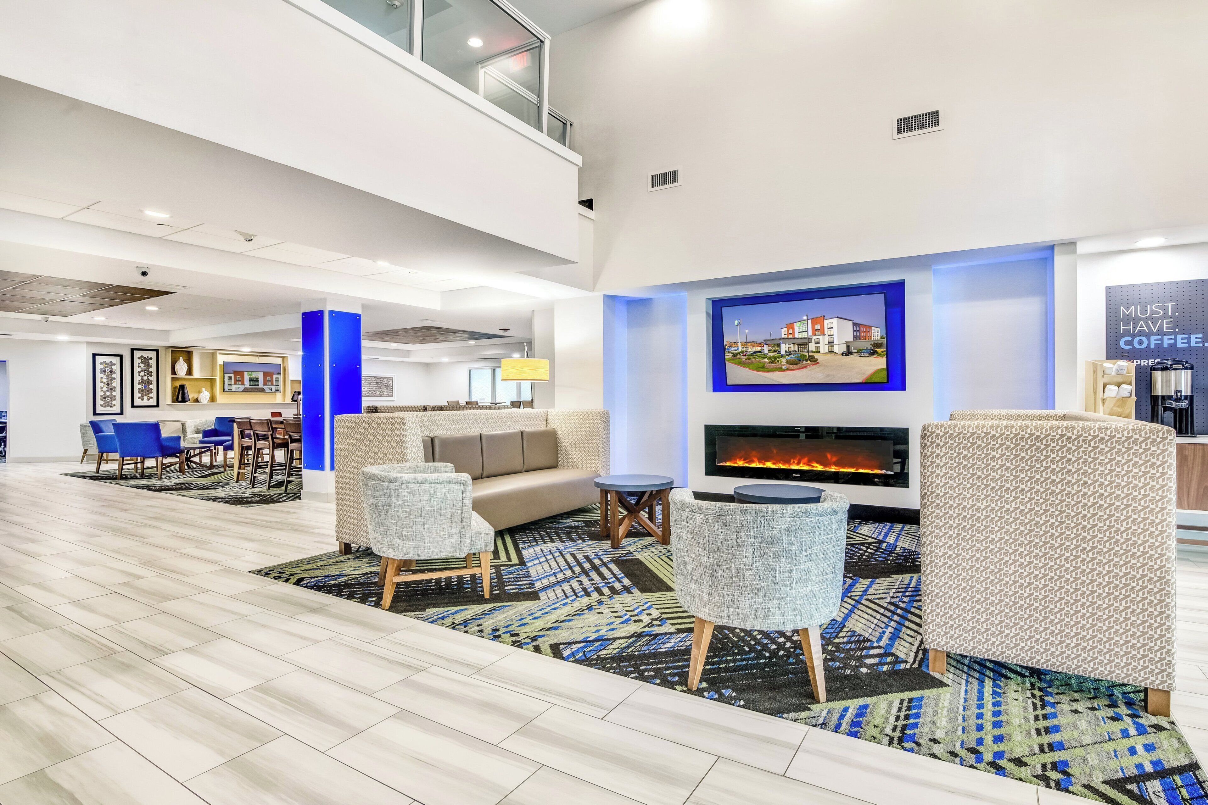 A modern lobby with a seating area, a fireplace, and a coffee station.